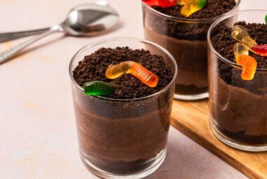 Three dirt pudding cups, topped with gummy worms and a side spoon.