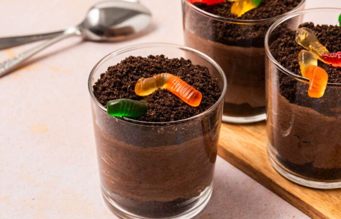 Three dirt pudding cups, topped with gummy worms and a side spoon.