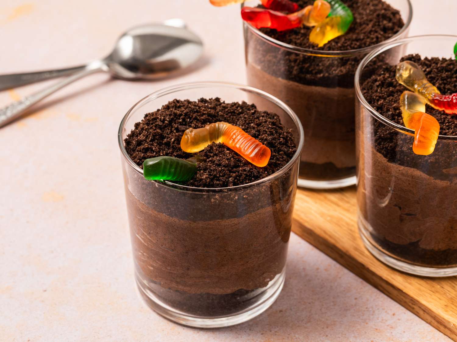 Three dirt pudding cups, topped with gummy worms and a side spoon.