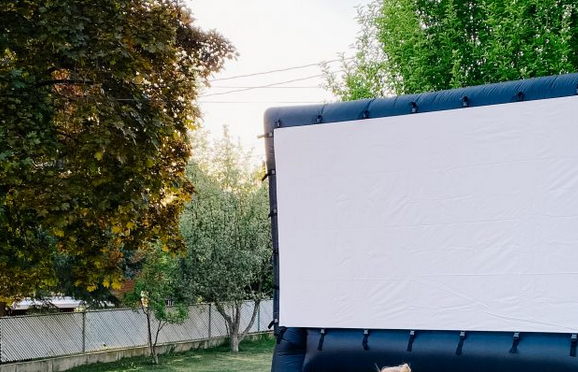 A black blowup screen setup in a backyard surrounded by trees
