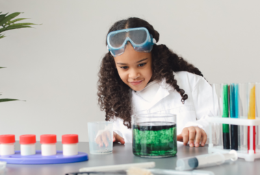 Elementary aged girl, in lab coat filling colored vials of water.