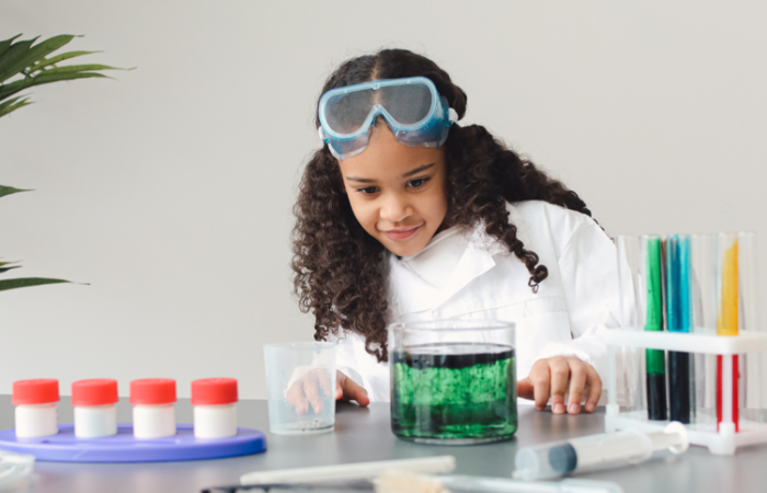 Elementary aged girl, in lab coat filling colored vials of water.