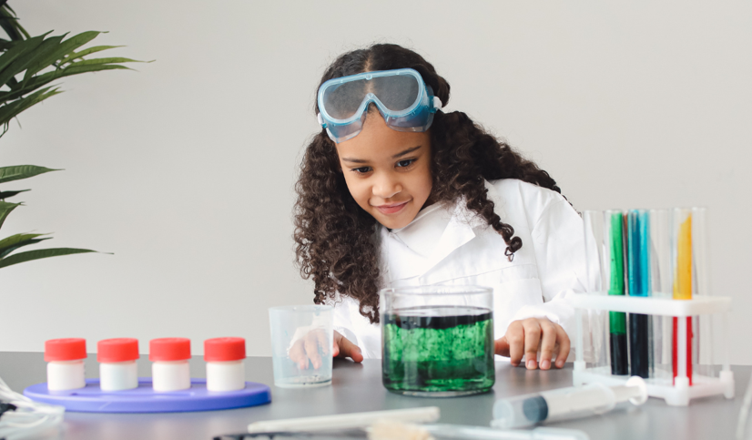 Elementary aged girl, in lab coat filling colored vials of water.